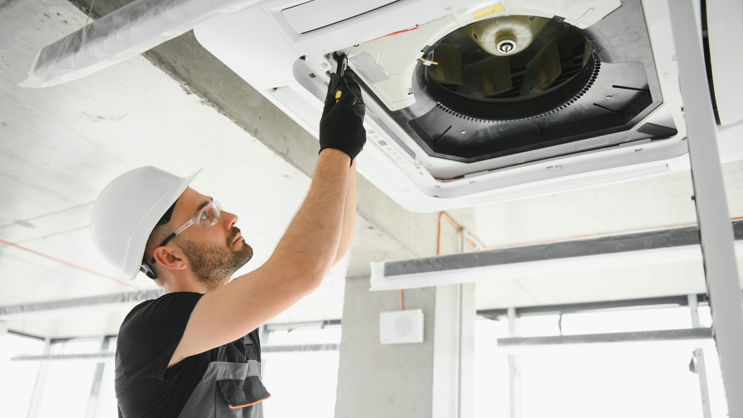 hvac-technician-installing-servicing-ceiling-air-conditioning-unit HVAC technician installing and servicing a ceiling air conditioning unit