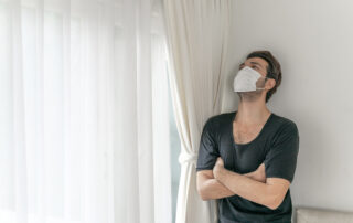 Man wearing a face mask to protect himself, feeling sick with headache and cough because of coronavirus COVID-19 in a quarantine room